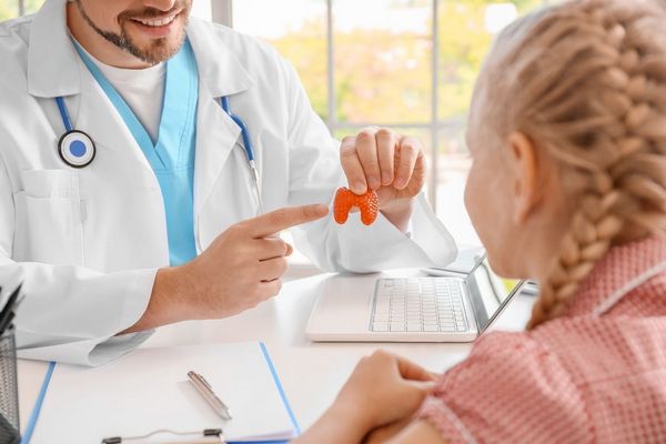 Egy fehér köpenyes orvos egy műanyag pajzsmirigyet mutat egy kislánynak.