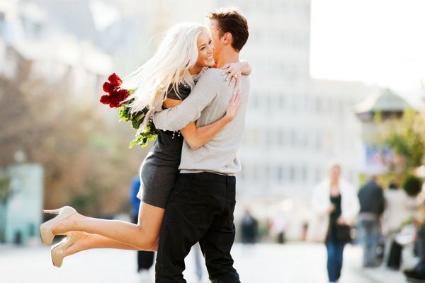 Egy fiatal pár ölelik egymást, a férfi vörös rózsacsokorral köszöntötte a szőke feleségét.