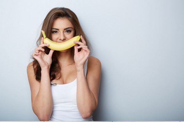 Egy fiatal lány banánt tart a szája elé, banánnal mosolyog.