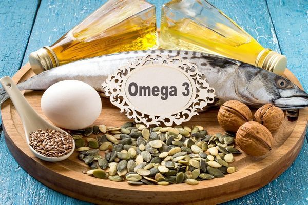 Egy fatálon omega-3 felirat, üvegekben olajok, mellettük, dió, hal, tojás, kanálban lenmagok és tökmagok.