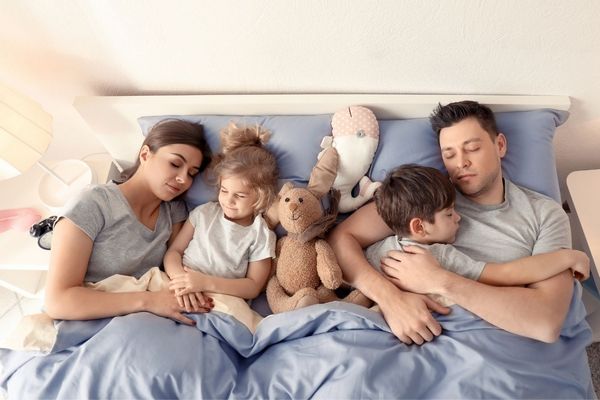 Egy ágyban egy család alszik, anya, apa és két gyermekük.
