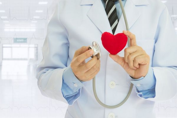 Egy fehér köpenyes orvos fonendoszkópot és egy piros műanyag szívet tart a kezében.