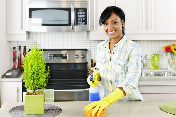 Fiatal nő a konyhában sárga gumikesztyűben takarít.