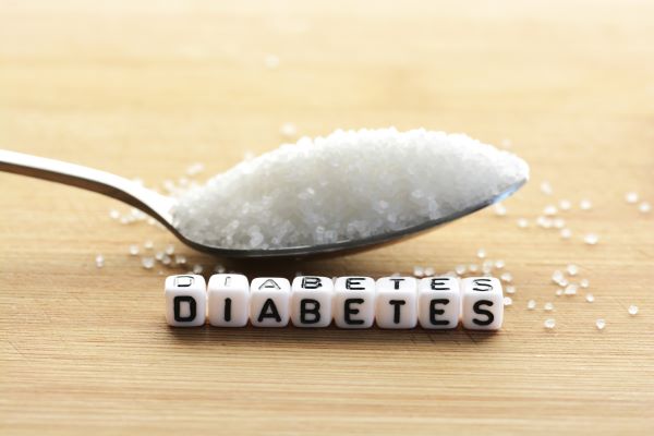 Asztalon egy púpozott evőkanál kristálycukor, előtte kis betűkockákból kirakva az angol "diabetes" szó.