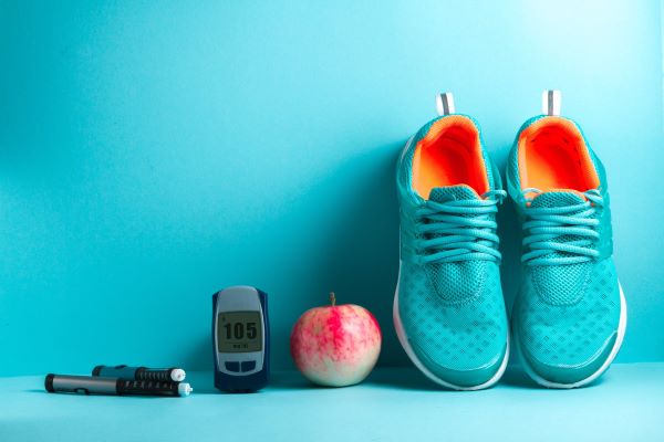 Kék háttér előtt vércukormérő, egy alma, egy pár kék sportcipő.
