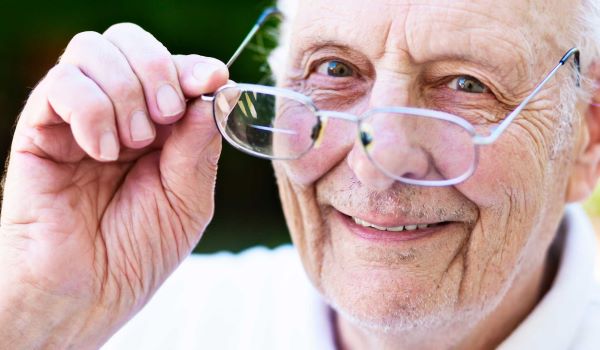 Idős férfi jobb kezével veszi le a szemüvegét.