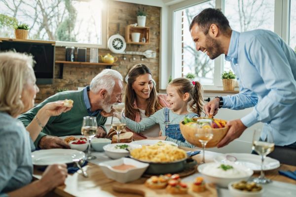 Családi étkezés az asztalnál: nagymama, nagypapa, anyuka, apuka és egy kislány vidáman eszeget és beszélget.