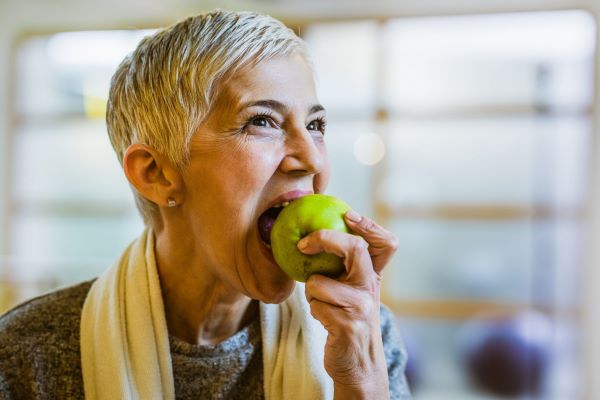 Rövid ősz hajú nő beleharap egy zöld almába.