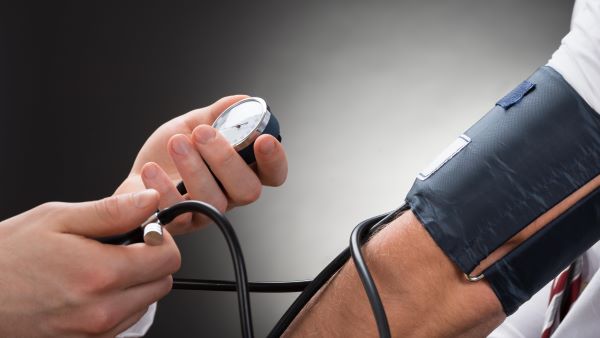 Férfi karon vérnyomásmérő, melynek vége női kezekben van.