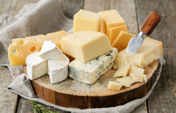 Faasztalon fatörzsszeleten különféle sajtok és sajtkés.