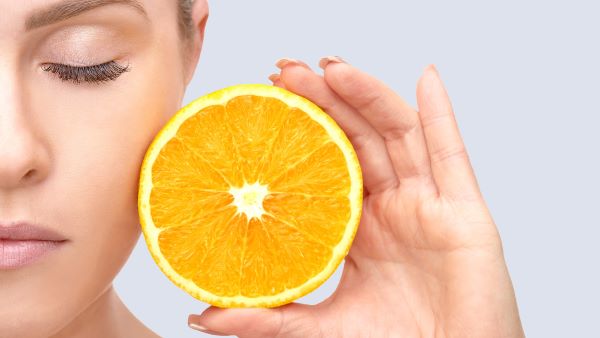 Fiatal nő csukott szemmel az arcához érint egy fél narancsot.