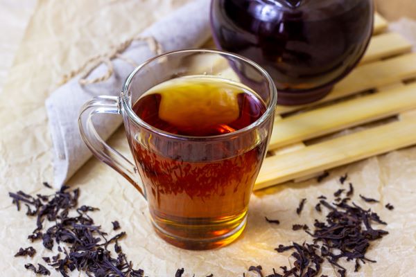 Kancsóban és üvegpohárban tea, mellette kiszórva teafű.
