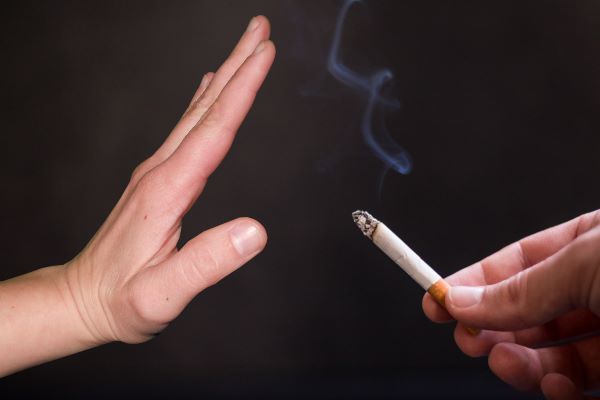 Fekete háttér előtt égő cigarettát kínáló kéz, melyet egy másik kéz elhárít.