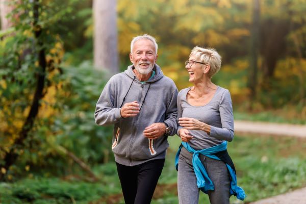 Idősebb férfi és nő tréningruhában vidáman futnak az erdőben.