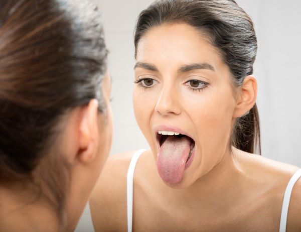 Fiatal nő a tükörrel szemben kinyújtott nyelvvel nézi a nyelvét.