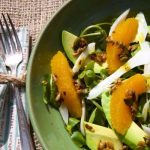 Zöld tányérban avokádós-édesköményes-mandarinos saláta, mellette szalvéta villával összekötözve.
