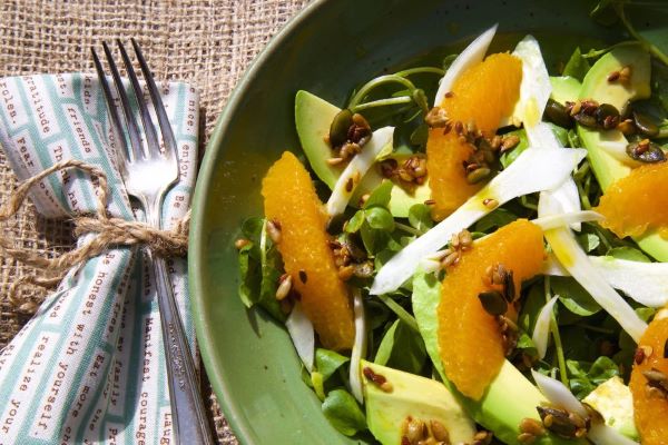 Zöld tányérban avokádós-édesköményes-mandarinos saláta, mellette szalvéta villával összekötözve.