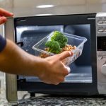 Mikrohullámű sütőbe egy férfi behelyez műanyag dobozban lévő ételt.