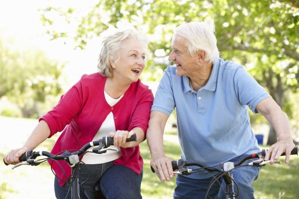 Idős nő és férfi biciklin ülnek egymás felé fordulva vidáman.