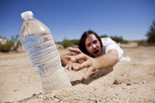 Sivatagban egy férfi a homokban fekve nyúl egy teli ásványvizes palack után.