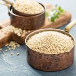 Nyeles fémedénykében quinoa, háttérben vágódeszkán újabb edényben quinoa.
