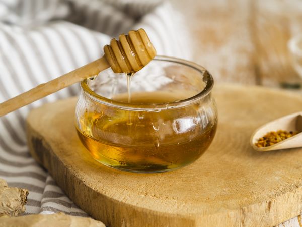 Fakorongon üvegtálkában méz, melybe egy mézpergetőről csurog a méz.
