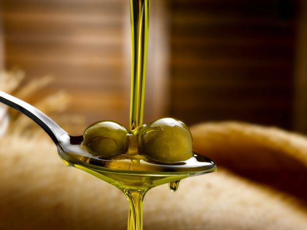 Olívaolaj csurog egy kanálra, amelyben két zöld olívabogyó van.