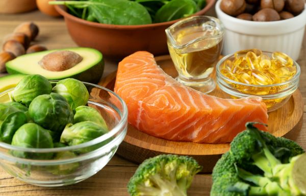 Omega-3 zsírsavakat tartalmazó ételek és omega-3 kapszulák az asztalon: lazac, avokádó, kelbimbó, brokkoli, spenót.