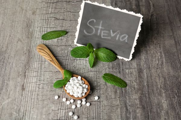 Faasztalon fekete tábla "stevia" felirattal, fakanálban fehér tabletták, néhány zöld levél.
