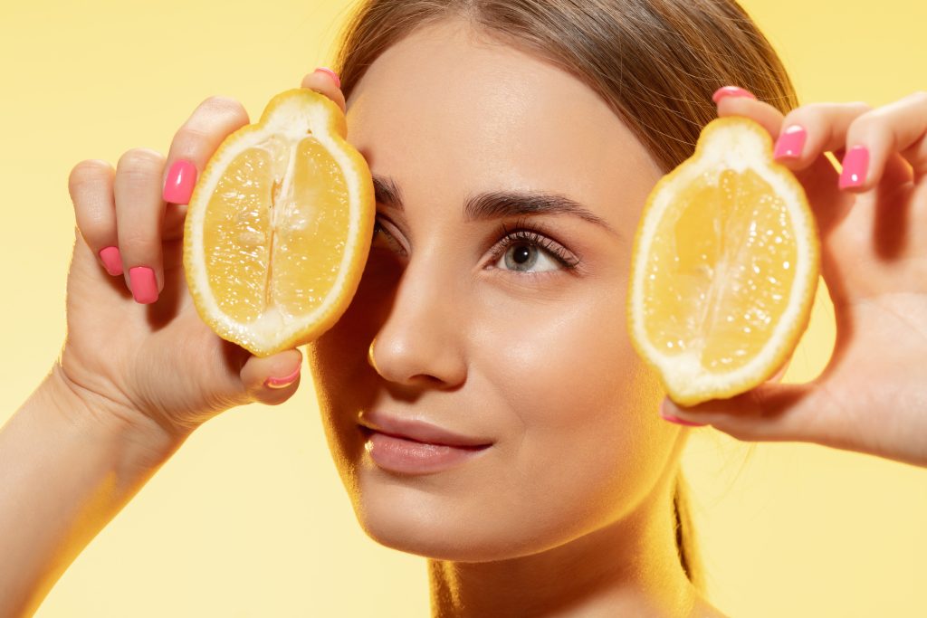 Fiatal nő az arcához tart két fél citromot.