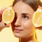 Fiatal nő az arcához tart két fél citromot.