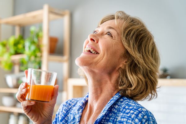 Idősebb nő nevetve tart a kezében egy pohár gyümölcslét.