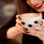 Mosolygó nő fehér csészét tart a kezében, mely tele van kávéval.