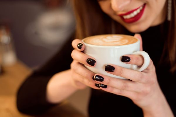 Mosolygó nő fehér csészét tart a kezében, mely tele van kávéval.