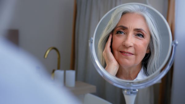 Idősebb nő arcának tükörképe egy kerek asztali tükörben.