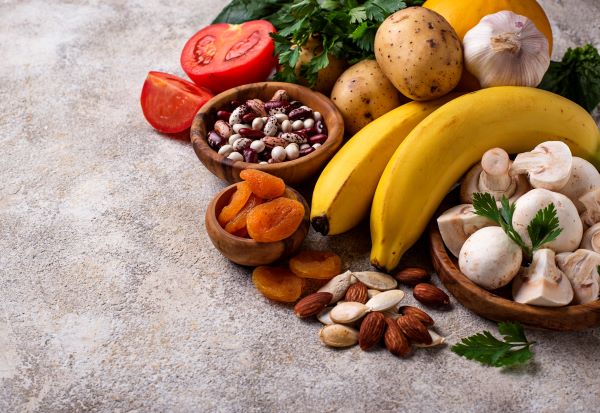 Káliumot tartalmazó élelmiszerek a konyhapulton: bab, burgonya, paradicsom, banán, gomba, mandula, fokhagyma, aszalt sárgabarack.