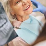 Idős nő fogsorát és röntgenfelvételét vizsgálja a fogorvos.