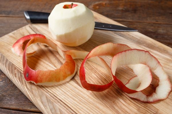 Vágódeszkán egy hámozott alma, almahéj és kés.