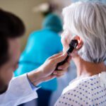 Idős nő fülét vizsgálja egy szakállas orvos.