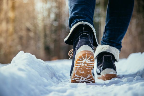 Sétáló nő bakancsos lábai a hóban közelről.