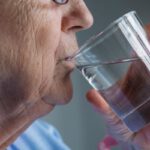 Közeli fotó idős nőről, aki egy pohár vizet iszik.