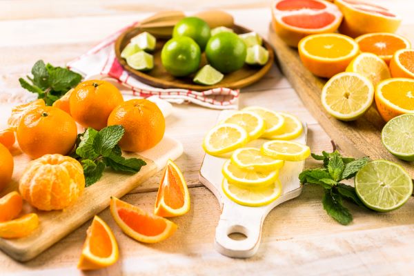 Faasztalon vágódeszkákon egész és félbevágott, illetve szeletelt citrusos gyümölcsök: narancs, citrom, lime, mandarin, grépfrút.