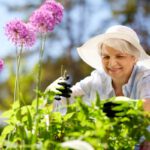 Idősebb nő fehér kalapban kertészkedik.