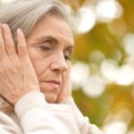 Idős nő mindkét tenyerét a füleire tapasztja.