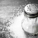 Üveg sószóró, körülötte só a sötét asztalon.