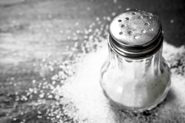 Üveg sószóró, körülötte só a sötét asztalon.