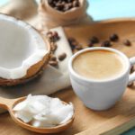 Ovális fatálon egy csésze kávé, körülötte kávébabszemek, mellette egy darab kókuszdió, fakanálban kókuszhús,