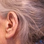 Közeli fotó idős nő egyik füléről és ősz hajáról.