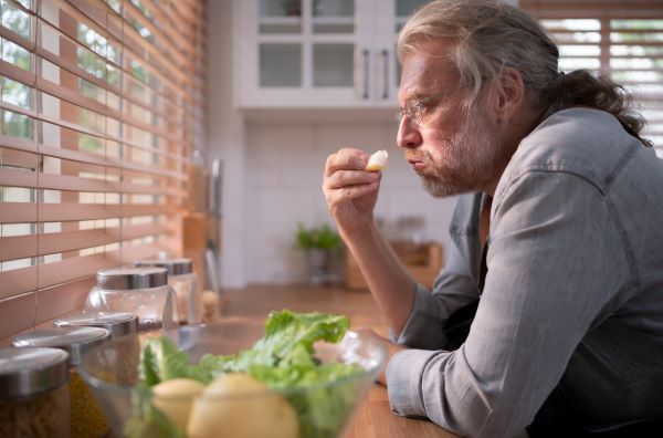 Középkorú férfi a konyhában a pultra könyökölve egy falat ételt tart a kezében.
