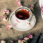 Virágos csészében tea rózsaszirmokkal, mellette virágos teáskanna, körülötte elszórva rózsabimbók.